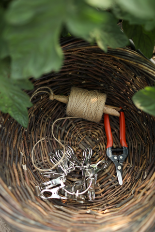 Jute tuintouw op houten klos in een oogstmand met oogstschaar en metalen plantenclips.